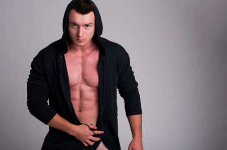 Handsome male model posing naked wearing a hoodie in studio at photo shootingの写真素材