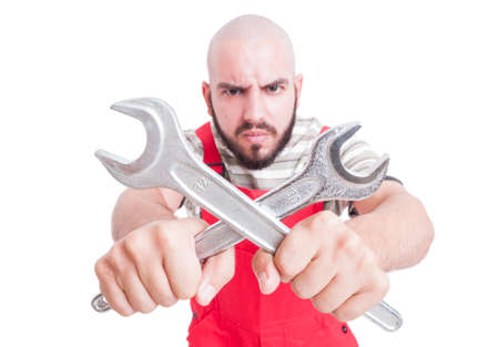 Angry mechanic or plumber holding crossed wrenches wearing red overall uniform isolated on whiteの写真素材