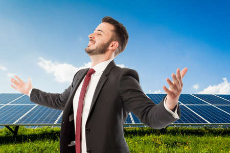 Happy smiling businessman with wide outspread or outstretched arms on solarpower photovoltaic panel backgroundの写真素材