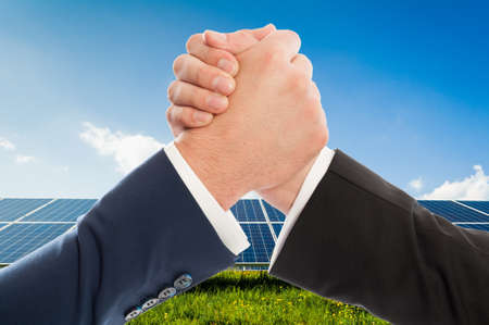 Businessmen handshake as teamwork on solarpower photovoltaic panel background. Renewable energy partnership agreementの写真素材