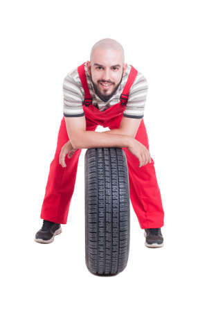 Happy mechanic resting on a new car wheel isolated on white studio backgroundの写真素材