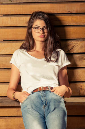 Adorable hipster female model on wooden fence background wearing eyeglassesの写真素材