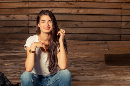 Cute female model smiling wearing jeans and t-shirt on wooden backgroundの写真素材