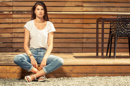 Gorgeous teen female model posing outdoor wearing jeans and t-shirt on wooden fence backgroundの写真素材