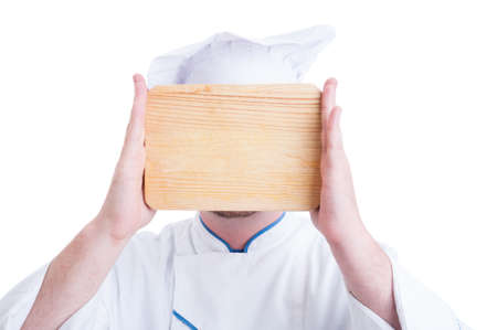 Chef or cook holding wooden chopping board covering his face isolated on whiteの写真素材