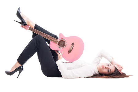 Beautiful young female guitarist lying down on white floor isolated on studio backgroundの写真素材