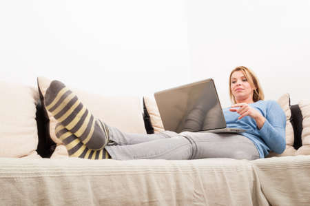 Beautiful woman chatting online or blogging using laptop on the couch at homeの写真素材