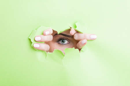 Woman eye with make-up looking thru ripped cardboard as beauty concept on advertising areaの写真素材