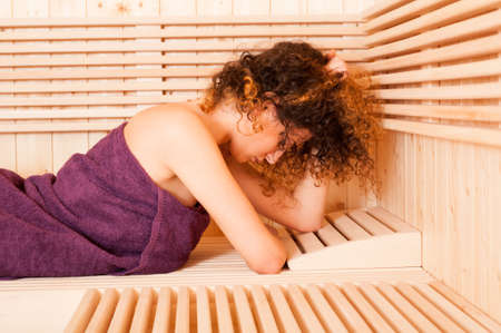 Close-up of pretty female holding her curly hair in a steam room with wooden benchの写真素材