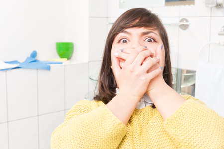 Close-up portrait of terrified woman scared at dentist visit sitting in chair and covering her mouthの写真素材