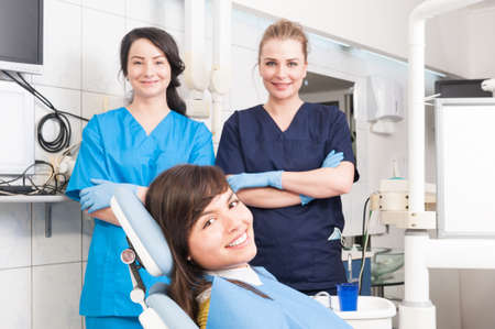 Portrait of smiling female dentist and assistant with female patient in the dentist chair as team work conceptの写真素材