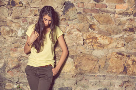 Attractive woman wearing modern casual clothes and posing near stone wall