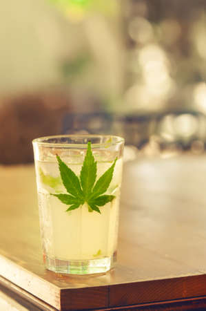 Close-up of glass with ice, alcohol and marijuana leaf on a table as stimulant substance concept