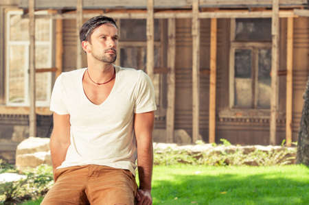 Young hipster male sitting outside on stone and posing  in trendy casual clothesの写真素材