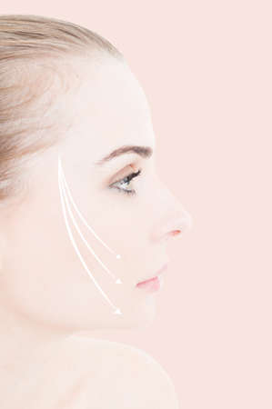 Close-up of woman face with lifting arrows on her cheek as facial beauty treatment and rejuvenation concept against pink backgroundの写真素材