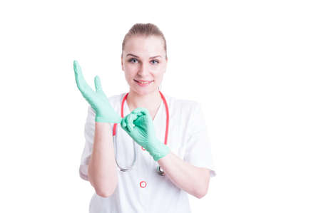Young female doctor in uniform putting on sterile latex gloves and smiling on white backgroundの写真素材