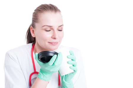 Close-up of beautiful female doctor enjoy a coffee with pleasure on her break and smile isolated on white backgroundの写真素材