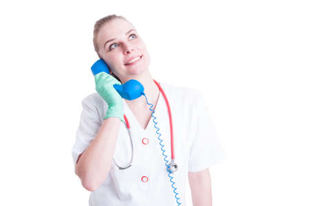 Cheerful woman doctor talking to a classic blue phone as medical appointment concept isolated on white backgroundの写真素材