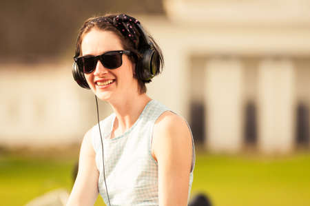 Young cheerful hipster woman listening to music in the park, smiling and relaxing outdoor