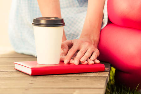 Close-up of a coffe and woman hands hold on red book as relaxation and freetime concept