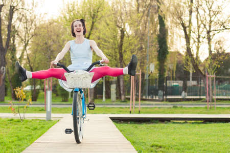 Cheerful woman in the park smiling and riding bicycle with her legs in the air and having funの写真素材