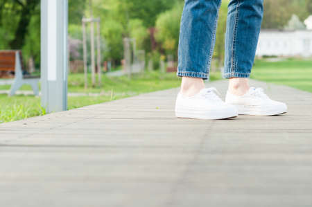 Woman feet with jeans and white casual shoes in closeup walking in the parkの写真素材