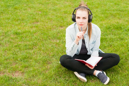 Young female thinking and writing while listening music outdoors on heandphones with copy spaceの写真素材