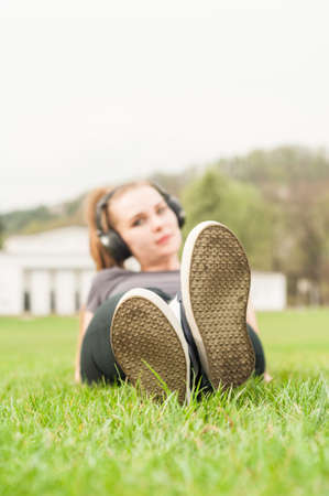 Young woman listening music on headphones while lying cross-legged on grassの写真素材