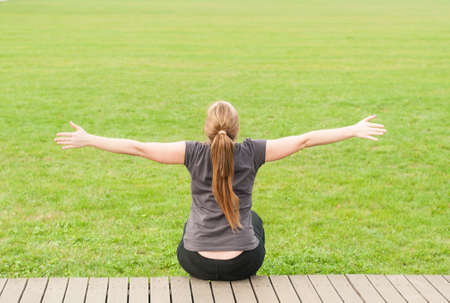 Young woman in back view sitting in the park with arms outstretched as happiness and freedom concept with copy spaceの写真素材