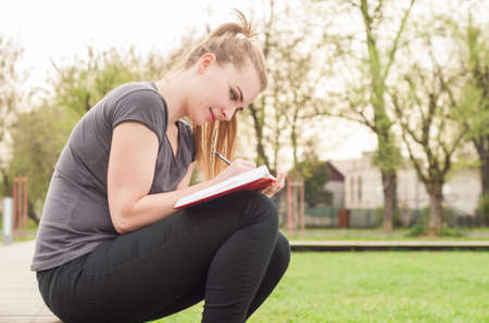 Joyful young female in spring park writing in her diary, relaxing and smilingの写真素材