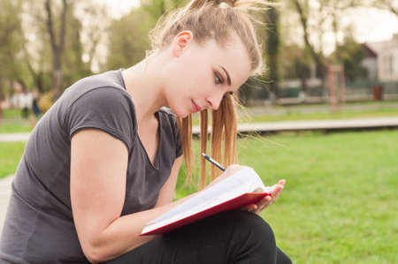 Attractive woman sitting outdoor and writes in her personal journal enjoying sunshine and freetimeの写真素材