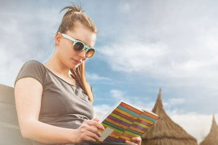 Young woman relaxing and reading a book on sunny day on the beach in her leisure time as  summer...