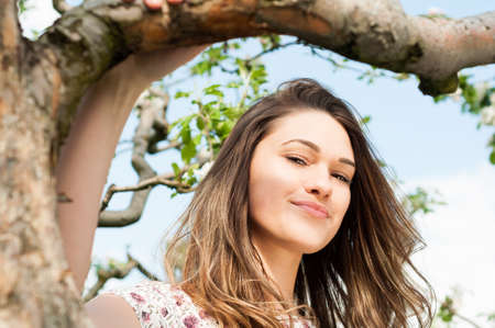 Spring girl outdoor portrait in blooming apple trees relaxing in sunny warm dayの写真素材