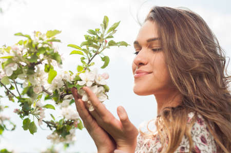 Spring beauty girl enjoying nature and sunshine in the blooming garden of apple treesの写真素材