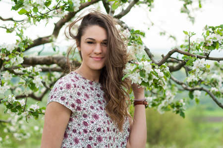 Romantic young woman portrait in blooming spring season sitting in apple tree garden full of white...