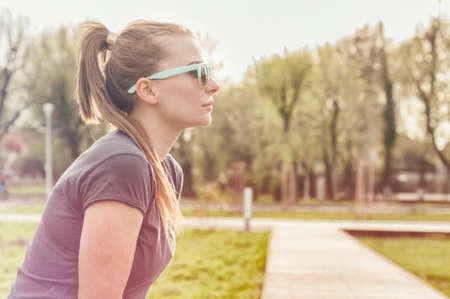 Profile of attractive young female wearing modern sunglasses resting in the park with copy spaceの写真素材