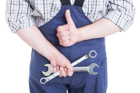 Closeup of mechanic showing thumbup behind his back and holding mechanical tools isolated on white