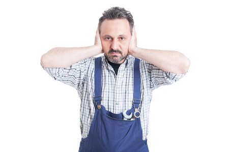 Young attractive mechanic covering his ears with hands as hear no evil concept isolated on white