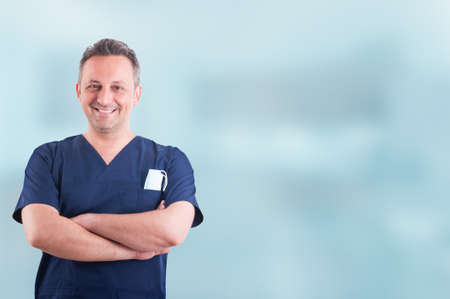 Cheerful attractive medic standing with folded arms and posing against blue background with copyspaceの写真素材