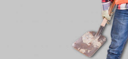 Renovation concept with young builder holding a shovel and wearing protection equipment with copyspace against grey backgroundの写真素材