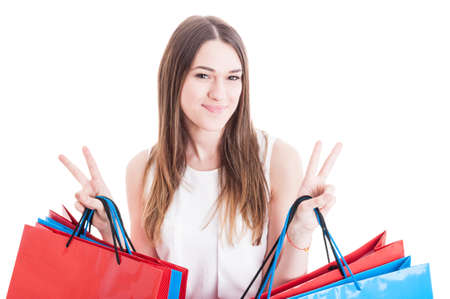 Joyful young girl doing shopping and showing double victory or peace sign isolated on white...