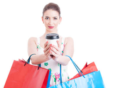 Attractive woman looking at camera and holding shopping bags offering takeaway beverage isolated on white background with copy text spaceの写真素材