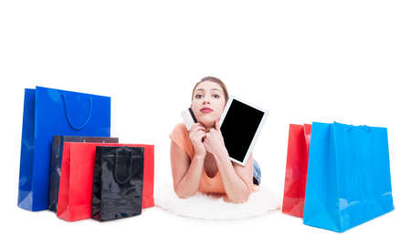 Lady laying around shopping bags and holding credit or debit card and tablet isolated on white...