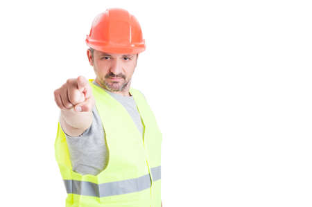 Young builder with orange hard hat working and pointing finger at you with copy space area isolated...