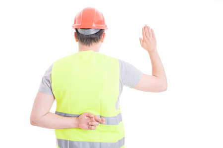 Young constructor taking oath with crossed fingers behind his back as dishonesty concept isolated on...