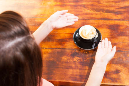 Woman sitting on terrace and showing coffee cup on wooden tableの写真素材