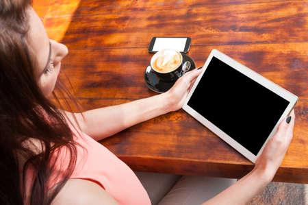 Woman holding tablet with coffee and smartphone aside outside on wooden terrace table with copy text space on blank screen or displayの写真素材