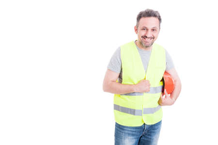 Cheerful male constructor with yellow vest holding his protection helmet isolated on white...