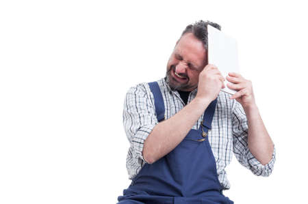 Angry repairman hitting head with digital tablet as frustration concept isolated on white background with copyspace areaの写真素材