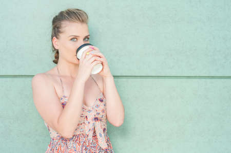Pretty girl drinking from takeaway coffee cup on green wall background with copy advertising area